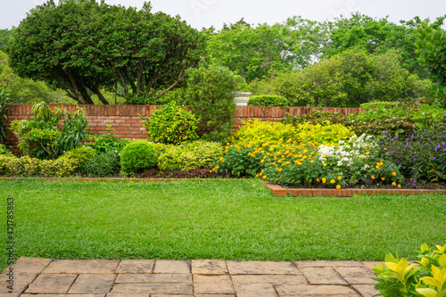 Slika na platnu Backyard English cottage garden on brown pavement and green lawn