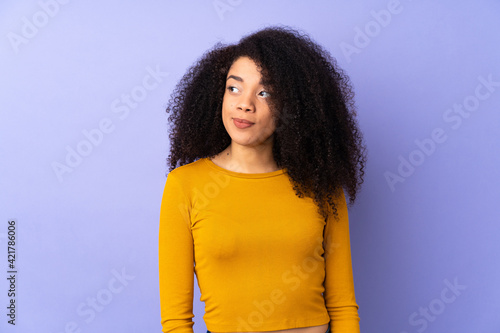 Young african american woman isolated on purple background making doubts gesture looking side © luismolinero