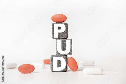 a group of white and red pills and cubes with the word PUD Peptic ulcer disease on them, white background. Concept carehealth, treatment, therapy. photo