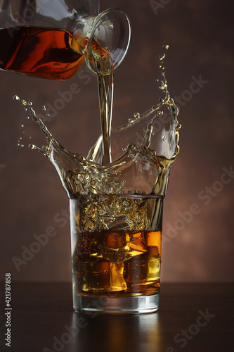 Pouring whiskey from bottle in to glass with ice cubes  on table