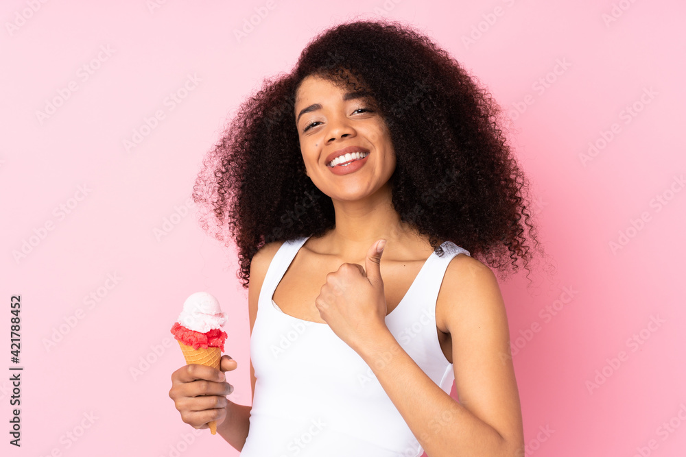 Young african american woman holding a cornet ice cream isolated on pink background with thumbs up because something good has happened Young african american woman holding a cornet ice cream isolated on pink background with thumbs up because something good has happened