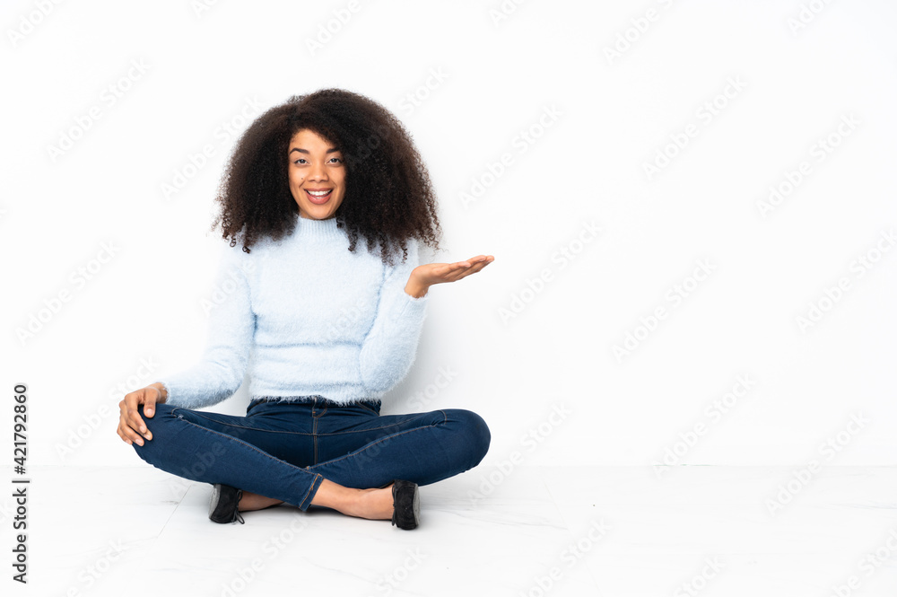Young african american woman sitting on the floor presenting an idea while looking smiling towards Young african american woman sitting on the floor presenting an idea while looking smiling towards