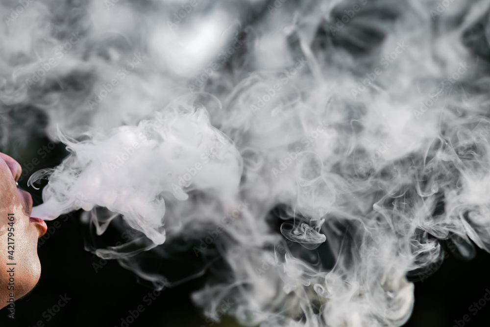 Close-up of a man spewing cigarette smoke from his mouth, black background, and space for text. Close-up of a man spewing cigarette smoke from his mouth, black background, and space for text.