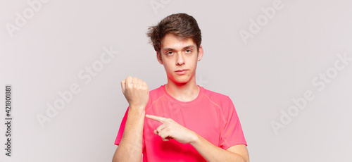 young boy looking impatient and angry, pointing at watch, asking for punctuality, wants to be on time photo