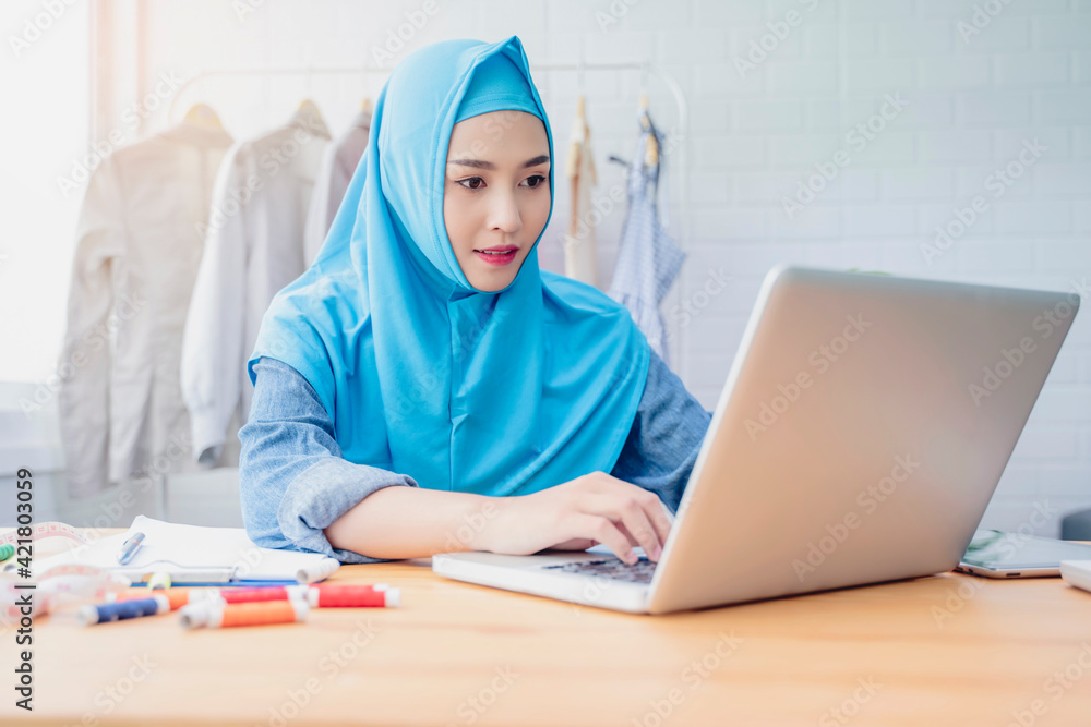 Asian Muslim woman fashion designer job occupation working in clothing textile workshop modern office researching design using computer laptop, designing planning using software application project Asian Muslim woman fashion designer job occupation working in clothing textile workshop modern office researching design using computer laptop, designing planning using software application project