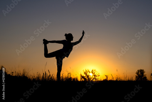 the silhouette of a girl meditating on one leg against the background of the setting sun