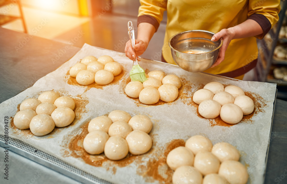 The baker greases the buns with sunflower oil for further baking. Automated production of bakery products. Bread factory. The baker greases the buns with sunflower oil for further baking. Automated production of bakery products. Bread factory.