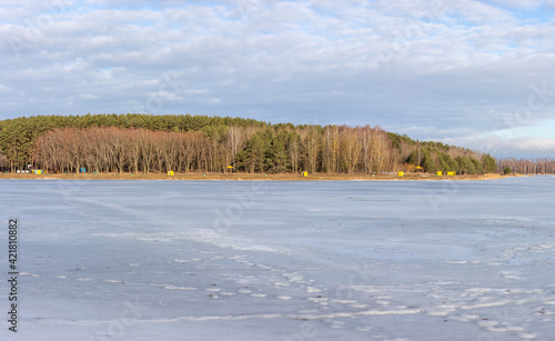 Cold winter sunny landscape. A large frozen lake  an empty beach on the far shore and beyond it a forest.