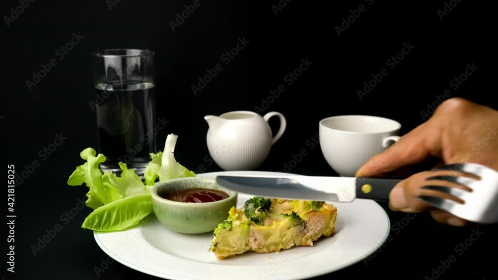 Senior hand using knife and fork for taking a bite of salmon fish and broccoli quiche in white ceramic dish. Senior hand using knife and fork for taking a bite of salmon fish and broccoli quiche in white ceramic dish.