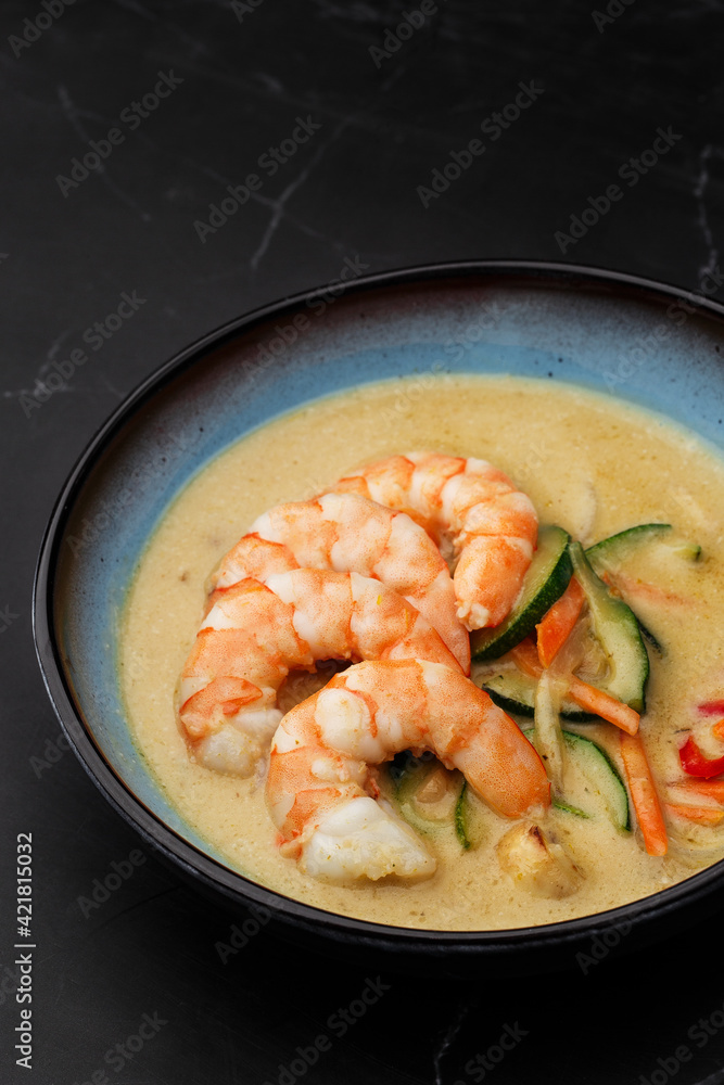Asian soup with shrimps and vegetables: zucchini, red pepper and carrot. Dish isolated in a blue bowl, close-up on a black marble background. Asian cuisine. Asian soup with shrimps and vegetables: zucchini, red pepper and carrot. Dish isolated in a blue bowl, close-up on a black marble background. Asian cuisine.