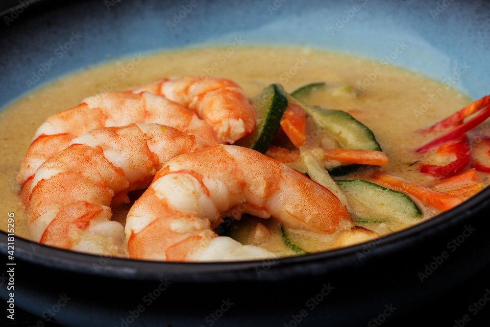 Asian soup with shrimps and vegetables: zucchini, red pepper and carrot. Dish isolated in a blue bowl, close-up on a black marble background. Asian cuisine. Asian soup with shrimps and vegetables: zucchini, red pepper and carrot. Dish isolated in a blue bowl, close-up on a black marble background. Asian cuisine.