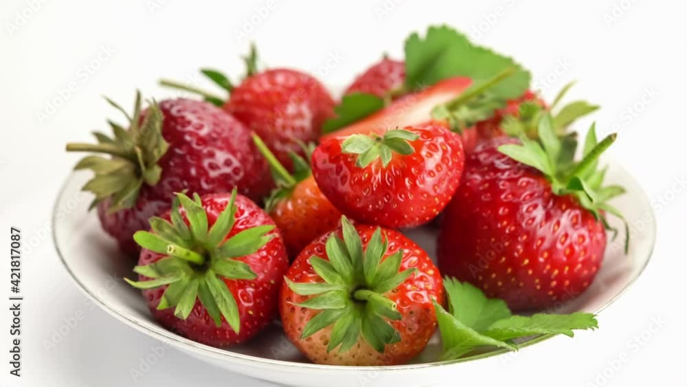 Side view pile of ripe strawberries with leaves in white ceramic dish turning on white background. Side view pile of ripe strawberries with leaves in white ceramic dish turning on white background.