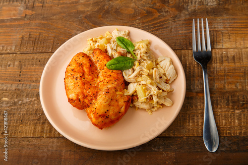 Baked chicken breast with salad on a plate next to a fork on a wooden table.