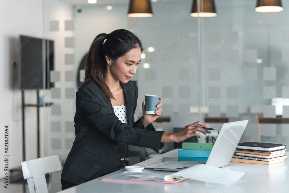 Asian businesswoman holding a coffee pointing at the laptop in the office. Asian businesswoman holding a coffee pointing at the laptop in the office.