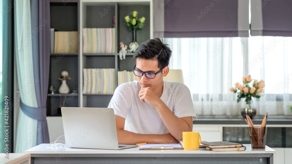 Young Asian man working at home using a laptop computer on a table. Young Asian man working at home using a laptop computer on a table.