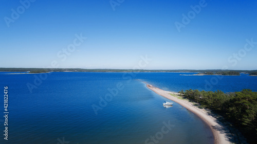  Top view of motorboat in blue water, bright sand beach, pine forest.