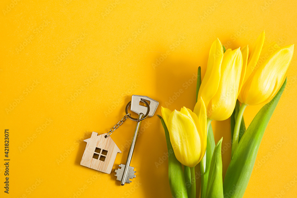 Key ring in the shape of wooden house with key on yellow background and spring tulips. Building, design, project, moving to new home, mortgage, rent and purchase real estate, summer offer. Copy space - obrazy, fototapety, plakaty 