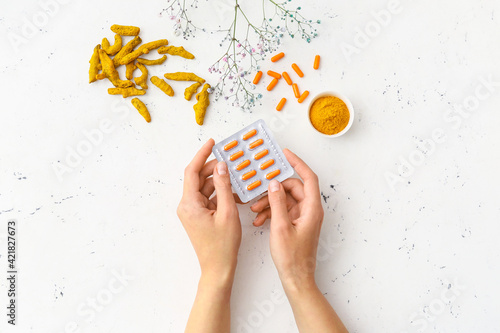 Fotografie Female hands and blister pack with turmeric pills on light background