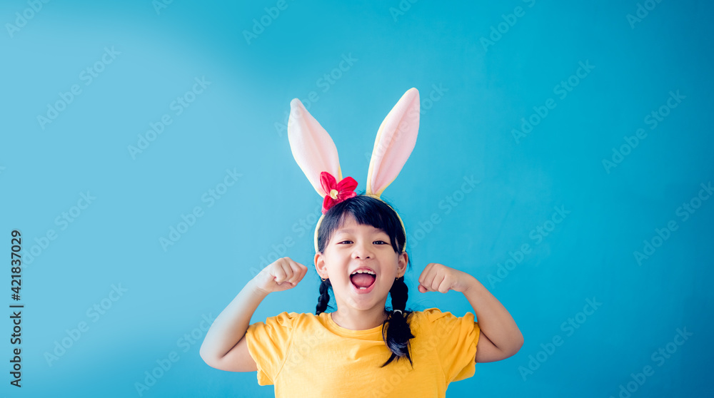 Cute little girl with bunny ears on color background.Strong superhero child.kid with muscles, milk, calcium.Kid Girl power in Easter day.Asian child kid girl background.Health care, immune system.