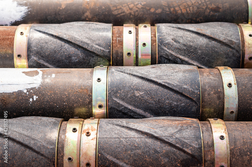 Stack of heavy steel drill pipe with reamer part that prepared for drilling to crude oil well in energy exploration industrial. Close-up and selective focus at center. Industrial object and equipment.