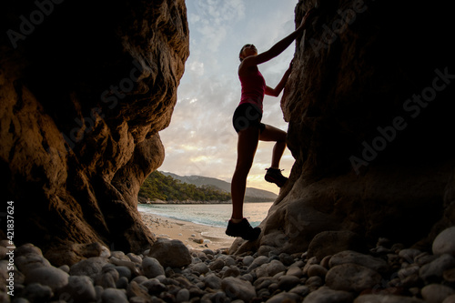beautiful silhouette of woman climbing on stones in gorge against the background of beach