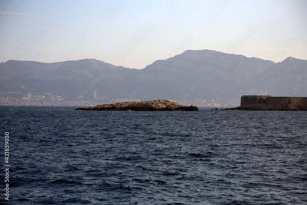 View of the city in the distance over the rocks outcropping from the sea, in the foreground, Parc National des Calanques, Marseille, France