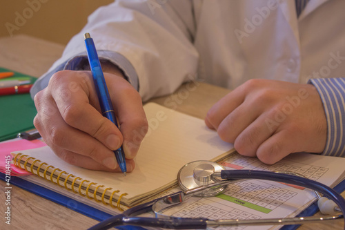 Male doctor with stethoscope sitting at a desk, writing something, prescription or recommendation of the patient, the photo