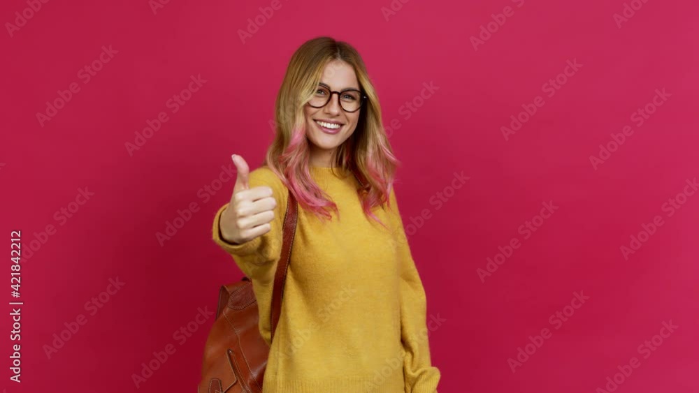 Young blonde woman with backpack giving thumbs up and smiling because something good has happened over isolated background Young blonde woman with backpack giving thumbs up and smiling because something good has happened over isolated background