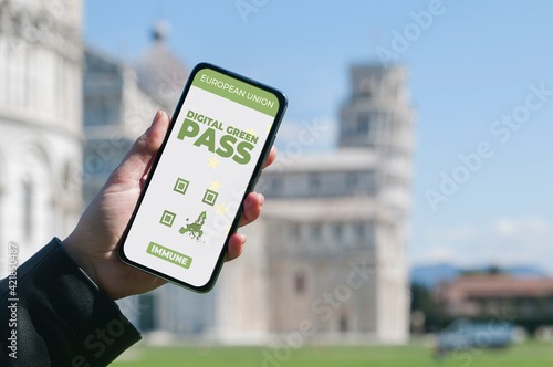 Digital Green Pass concept: Woman hold a smartphone in front of the Pisa leaning tower that show an hypotetical app for the Digital Green Passport (or digital pass certificate) photo