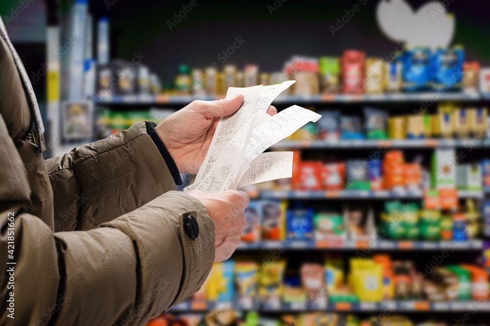 Minded man viewing receipts in supermarket and tracking prices - obrazy, fototapety, plakaty 