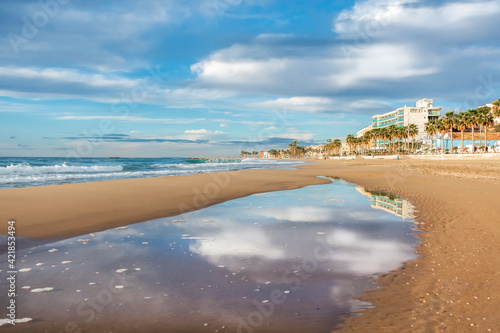 Villajoyosa beach with reflections of the clouds on a pool of water on the sand.