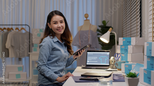 Portrait young attractive asia female owner startup business look at camera work happy with box at home prepare parcel delivery in sme supply chain, procurement, omnichannel commerce online concept.