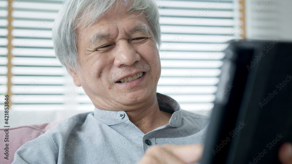 Candid old asian retired guy use tablet computer to transfer money online or financial payment and read text, smile or laugh with happy and positive. Senior asia with digital technology concept. Candid old asian retired guy use tablet computer to transfer money online or financial payment and read text, smile or laugh with happy and positive. Senior asia with digital technology concept.
