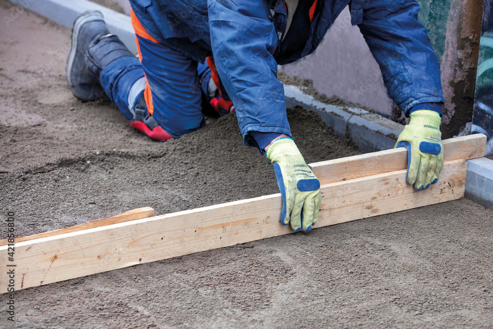 A squatting worker manually cleans and levels the sand base with a wooden plank for even tiling on the sidewalk. A squatting worker manually cleans and levels the sand base with a wooden plank for even tiling on the sidewalk.