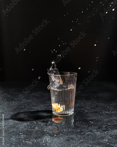 water with lemon in a glass on black background. Splaches