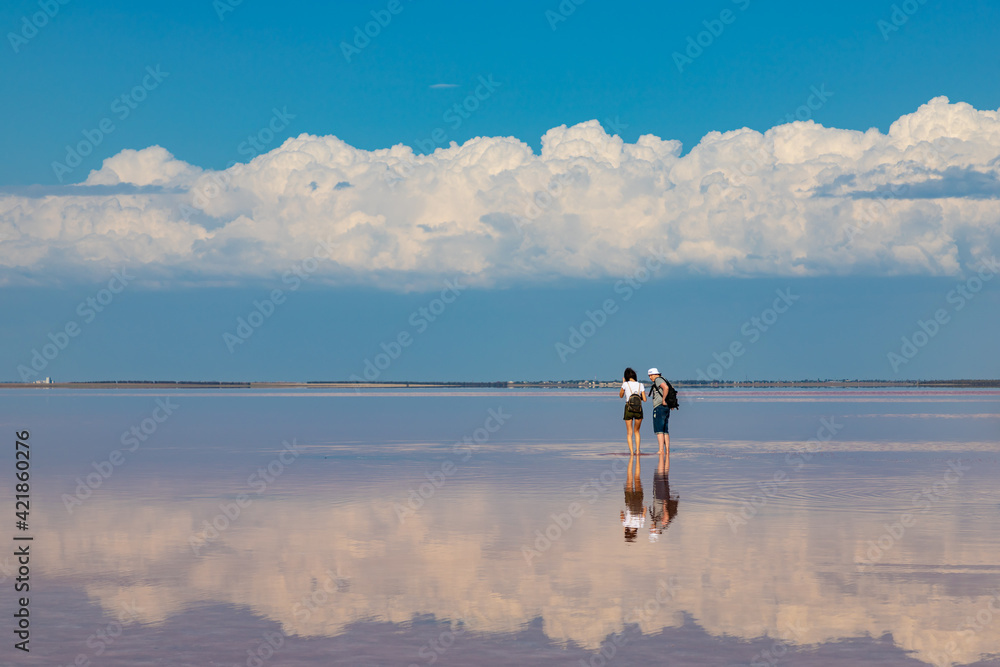 People walking at salt lake with pink salt and the blue sky with clouds. Sasyk-Sivash pink salt lake in Crimea. Summer landscape People walking at salt lake with pink salt and the blue sky with clouds. Sasyk-Sivash pink salt lake in Crimea. Summer landscape