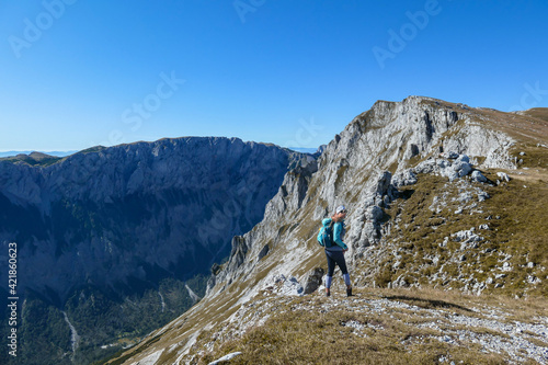 A woman with a hiking backpack standing at the edge of a high mountain, Hohe Weichsel in Austria. The woman in enjoying the view. Lush pasture around. Exploration and discovery. Endless mountain chain