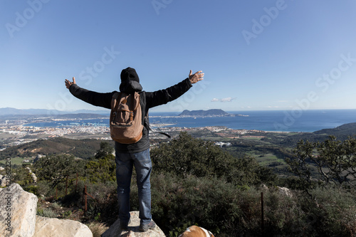 man dressed in winter clothes on top of a mountain contemplates with open arms the views of the bay of Algeciras and the rock of Gibraltar on a clear winter day