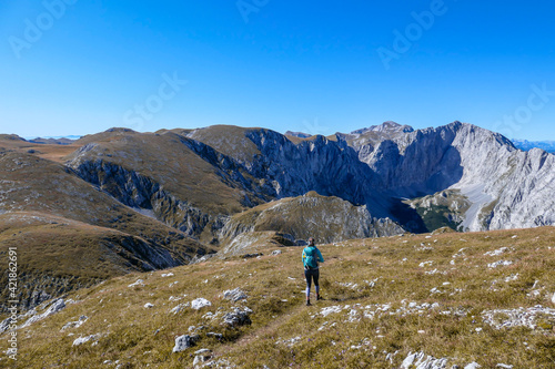 A woman with a hiking backpack hiking to the top of Hohe Weichsel in Austria. The woman in enjoying the calmness. The vast pasture is turning golden. Exploration and discovery. Endless mountain chains © Chris