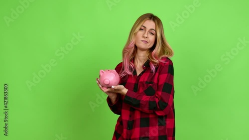 Young blonde woman happy and holding a piggybank over isolated background on green screen chroma key