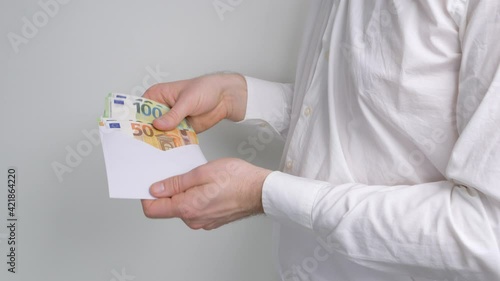 Business man receiving money like salary in a white envelope and looks into it. Euro banknotes used as payment in real life. Paying a worker for his job.