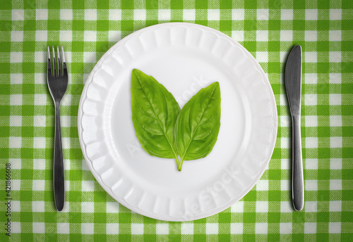 Vegan or vegetarian concept with green leafs on white plate against green checkered table cloth with fork and knife