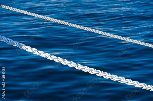 White marine mooring rope against background of blue water of Black Sea. Two white nautical cord. Background image of marine white rope in Sochi sea port. © MarinoDenisenko