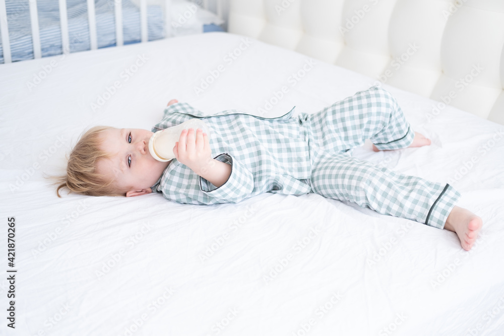toddler baby boy in pajamas lie on bed drinking milk from bottles. Candid home childhood life toddler baby boy in pajamas lie on bed drinking milk from bottles. Candid home childhood life
