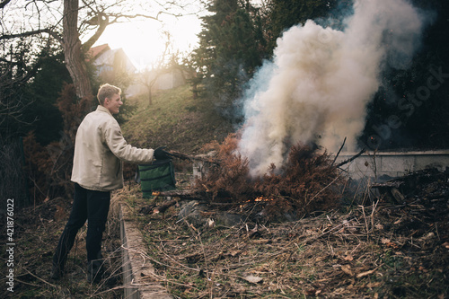 gardener man burning branch in fire pit during a summer revitalization of his garden