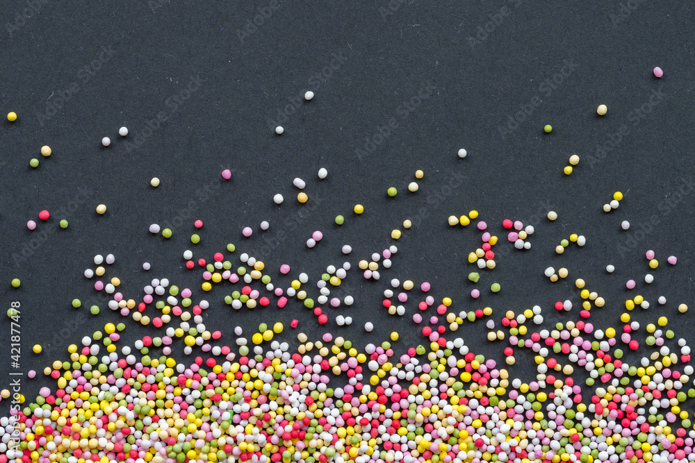 Rainbow ball-shaped sprinkles used as a topping for cakes isolated on black paper background