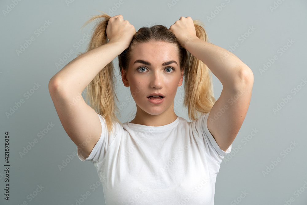 Girl with a shocking look on a gray background. Beautiful, young girl holding two ponytails from her hair.