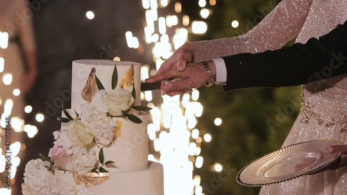 Cut the wedding cake. The bride and groom cut the wedding cake. Wedding cake with sparklers in several tiers. Detail of wedding cake cutting by newlyweds