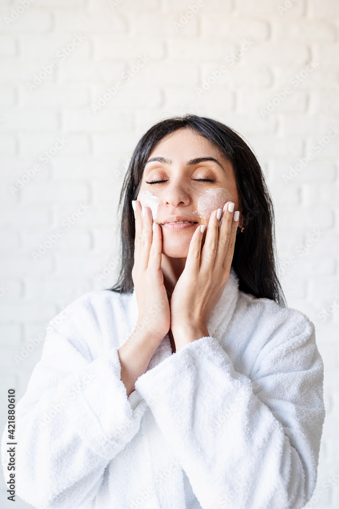 Happy beautiful middle eastern woman wearing bath towels applying facial cream on her face Happy beautiful middle eastern woman wearing bath towels applying facial cream on her face