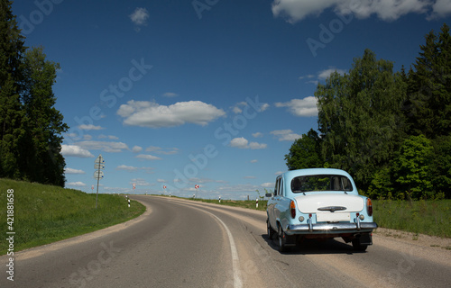 an old blue car is driving downhill against a blue sky